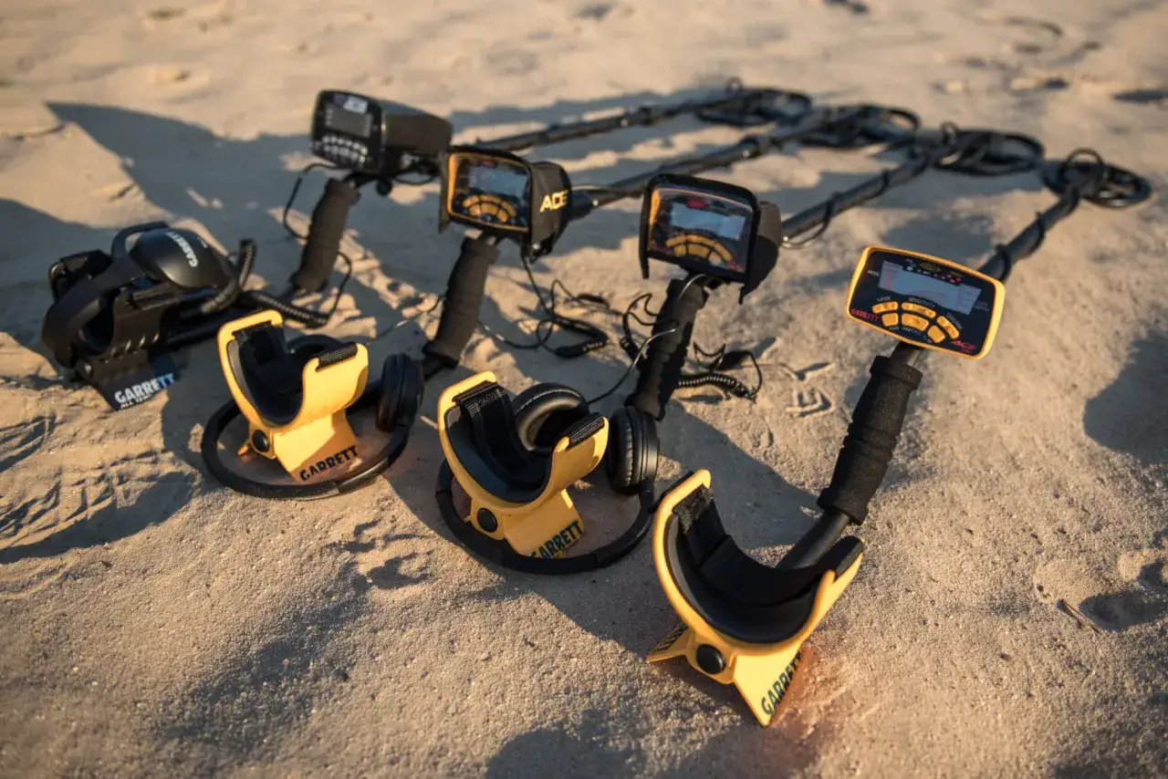 Kilka wykrywaczy metali Garrett leżących na piaszczystej plaży.