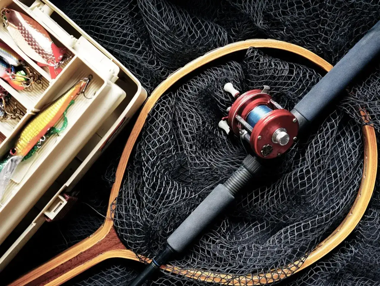 Wędka na grunt, czerwony kołowrotek, pudełko z przynętami i siatka. Idealny zestaw na jezioro.