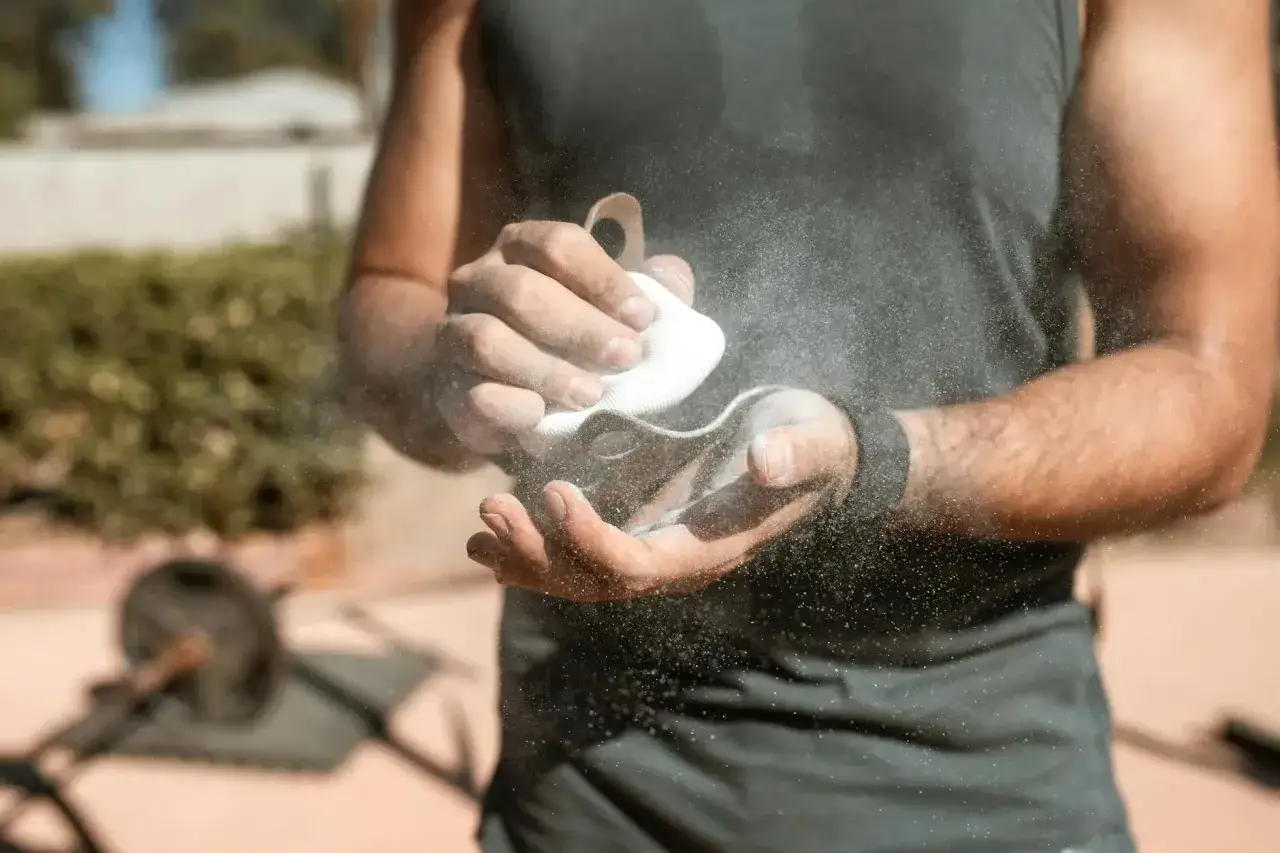 Dłonie sportowca posypane magnezją, która poprawia chwyt. To właśnie magnezja co to jest, pomaga w treningach siłowych i wspinaczce.