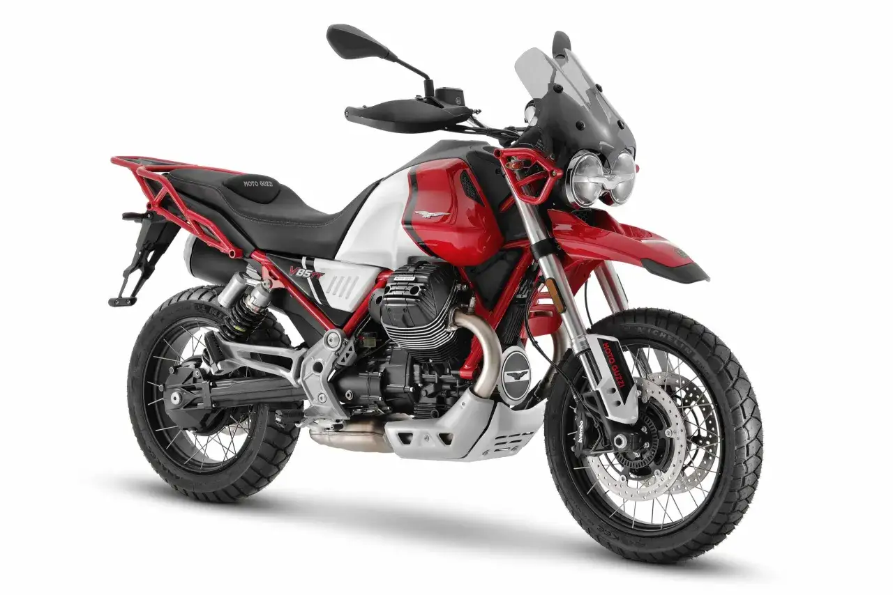 Czerwono-biały motocykl Moto Guzzi V85 TT z czarnym siedzeniem i akcentami, gotowy na przygodę.