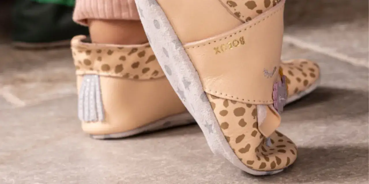 Beżowe kapcie dla dzieci z motywem panterki i gwiazdek, z ozdobnymi frędzelkami.