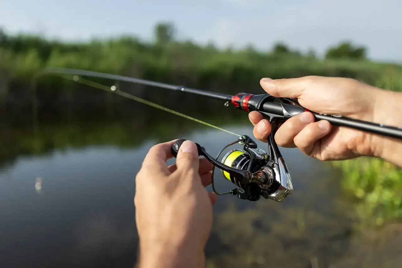 Dłonie trzymające wędkę spinningową i kołowrotek nad wodą.