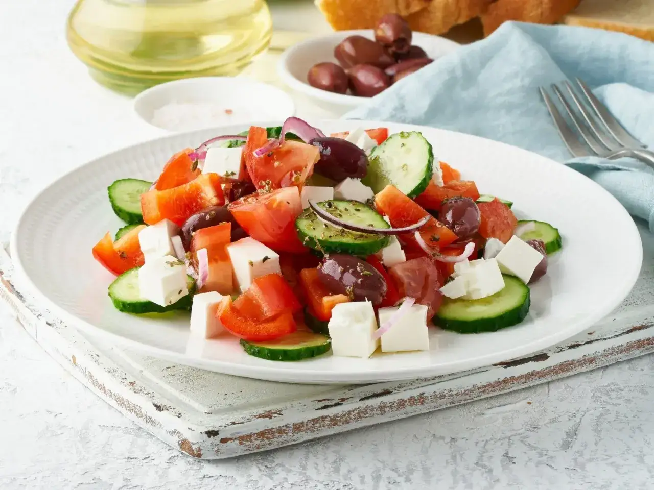 Sałatka grecka z pomidorami, ogórkiem, fetą, oliwkami i czerwoną cebulą na białym talerzu.
