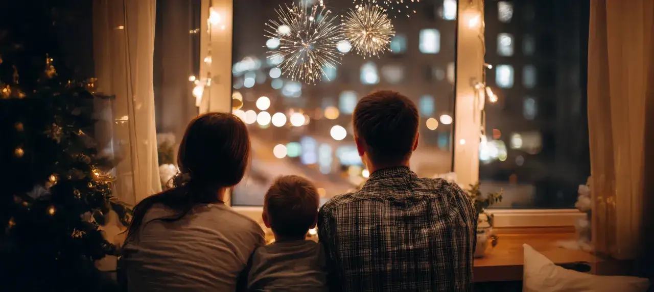 Rodzina ogląda fajerwerki przez okno. Wesoły sylwester z dziecmi, przy choince i lampkach.