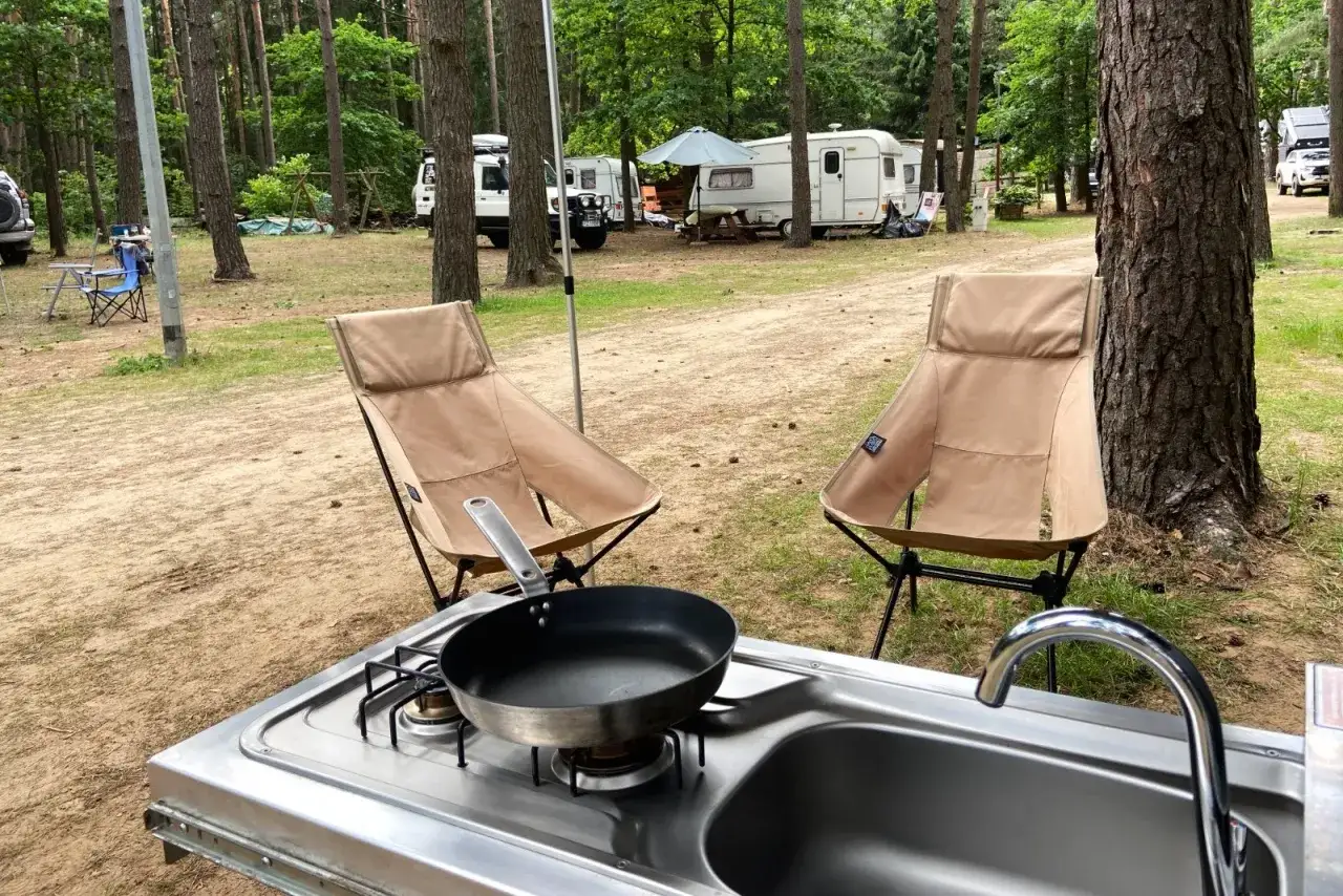 Kempingowy zestaw: kuchenka z patelnią, zlew i dwa krzesła w lesie.