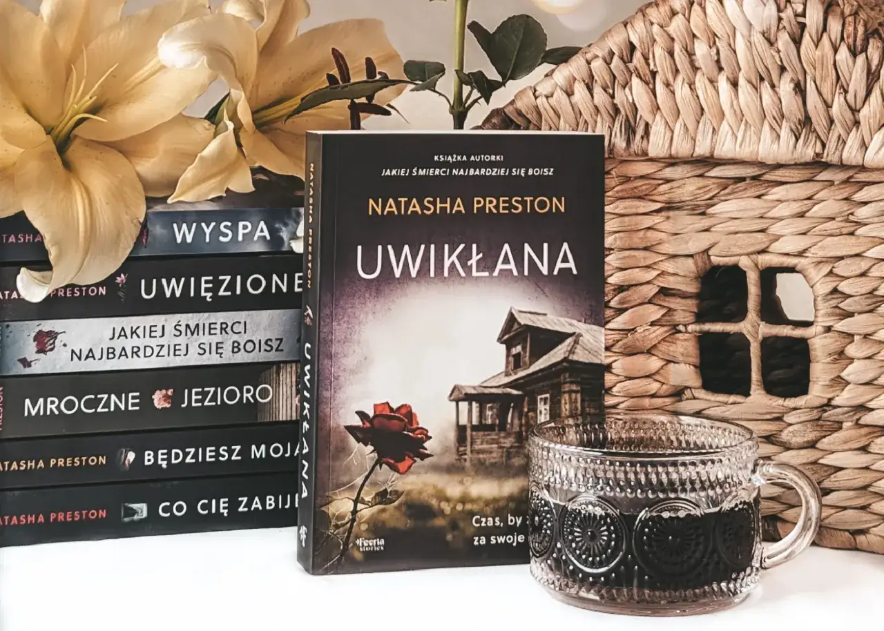 Stos książek z tytułem "Jakiej śmierci najbardziej się boisz", kwiaty, koszyk i kubek z napojem.