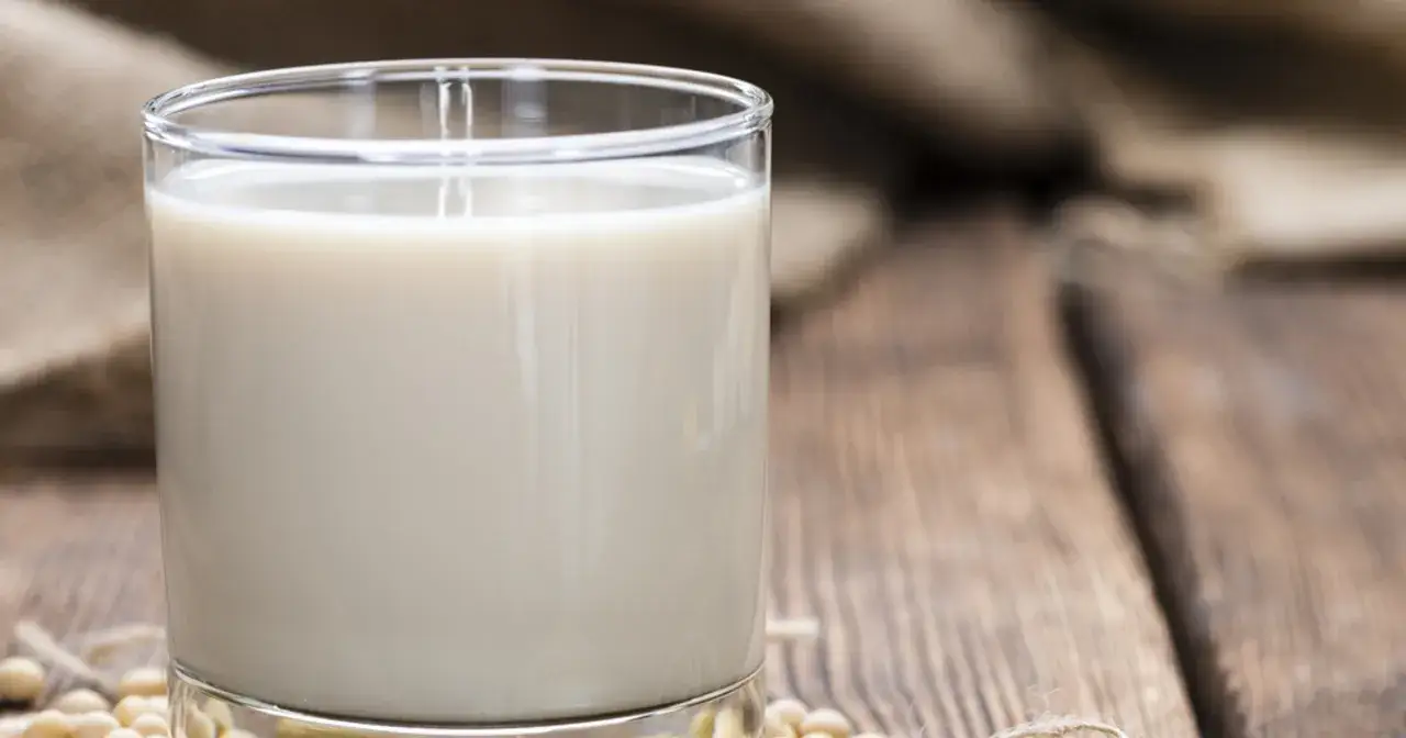 Szklanka mleka sojowego na drewnianym tle z ziarnami soi.