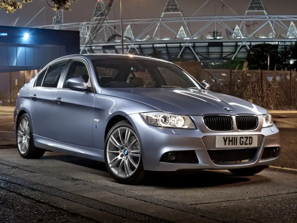 Srebrny sedan BMW E90 330d stoi na ulicy nocą, z tyłu widać stadion.