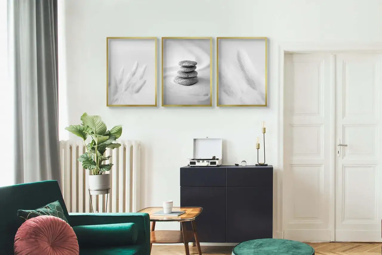 Trzy minimalistyczne plakaty w złotych ramach nad ciemną komodą. Dowiedz się, jak powiesić plakat bez niszczenia ścian.