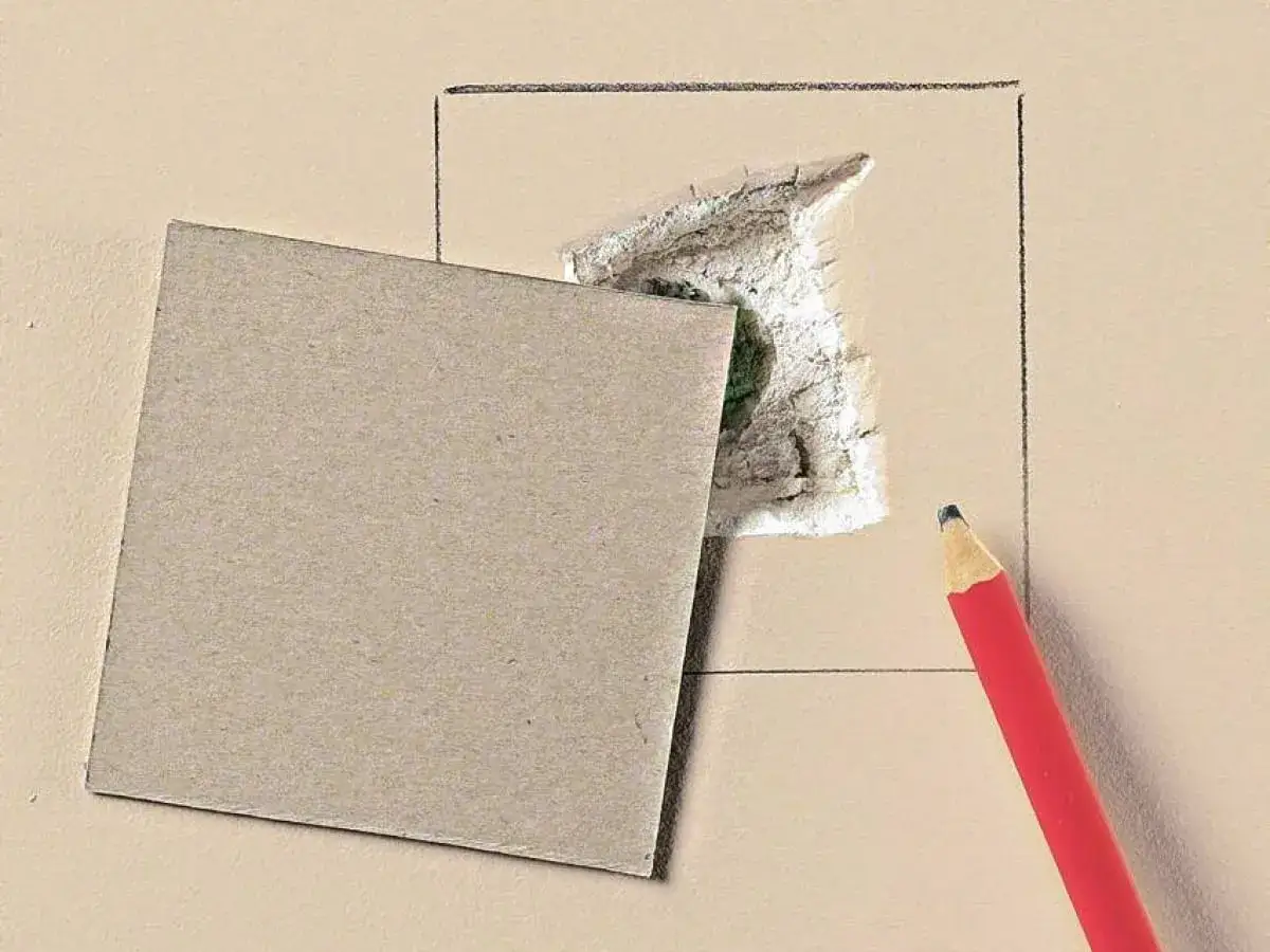 Kartonowy plaster i ołówek czekają, by pokazać, jak załatać dużą dziurę w ścianie.