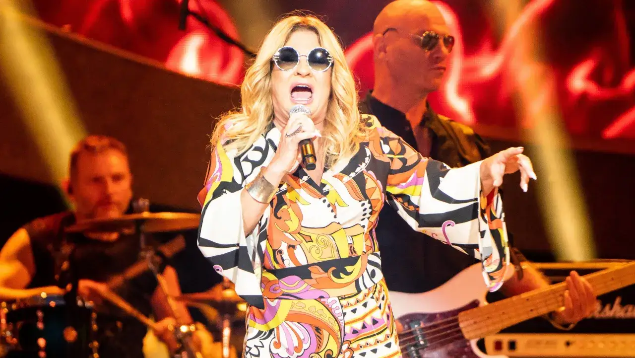 Wokalistka Bajm w kolorowej sukience i okularach przeciwsłonecznych śpiewa na scenie.