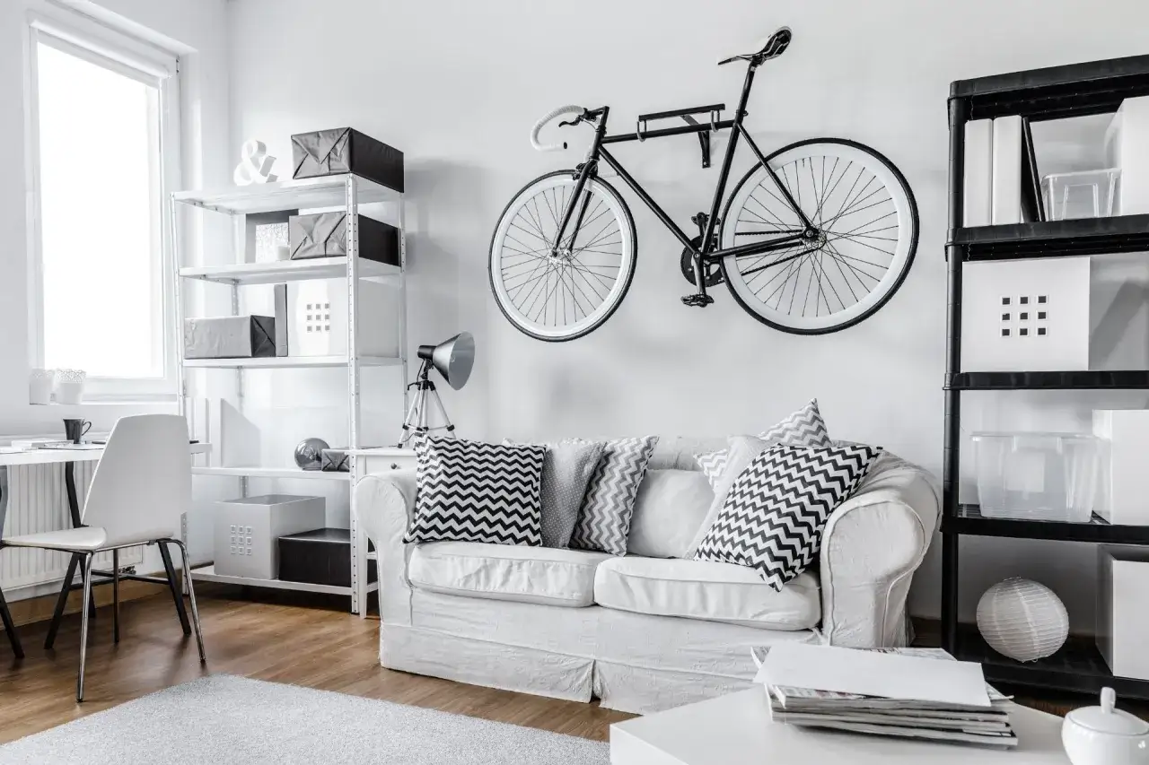 Nowoczesne przechowywanie rowerów na ścianie nad białą kanapą. Obok regały z pudełkami.