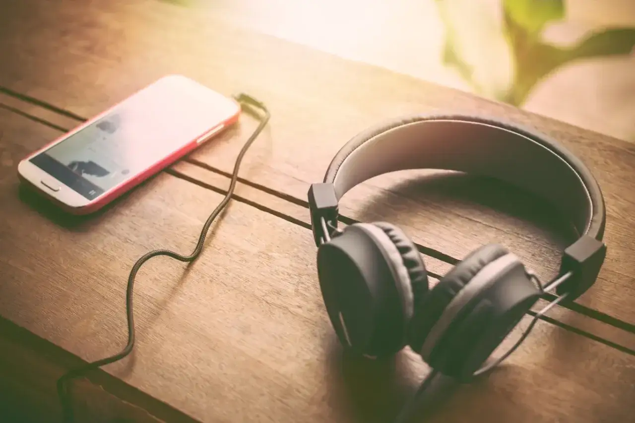 Słuchawki i smartfon leżące na drewnianym stole.
