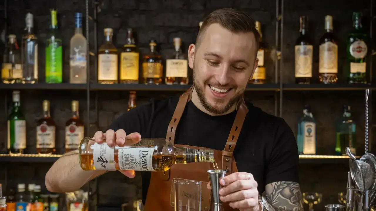 Uśmiechnięty barman, który robi drinki, nalewa whisky Dewar's do jiggera.