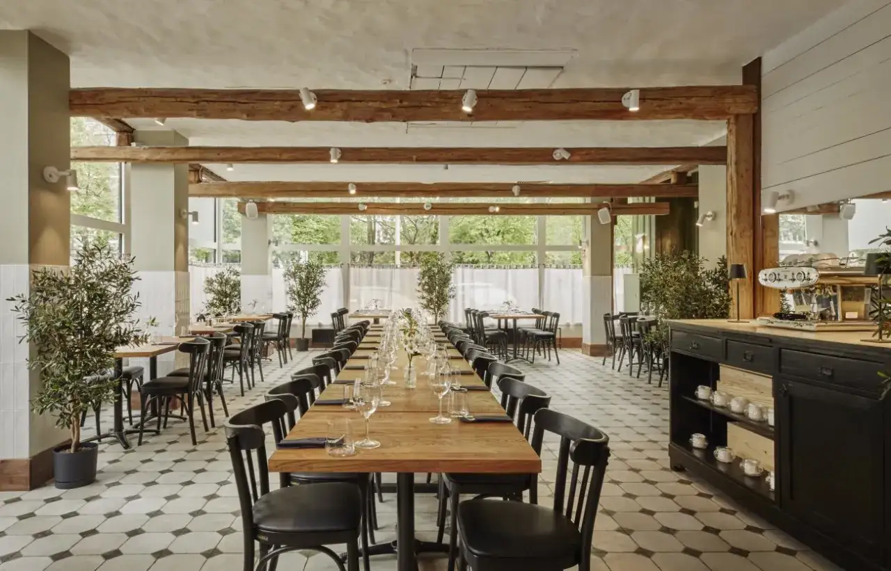 Elegancka sala restauracyjna z długimi stołami, idealna na degustację **primitivo kuchnia i wino**. Drewniane belki i duże okna tworzą przytulną atmosferę.