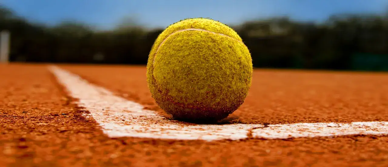 Piłka tenisowa na korcie, blisko białej linii.