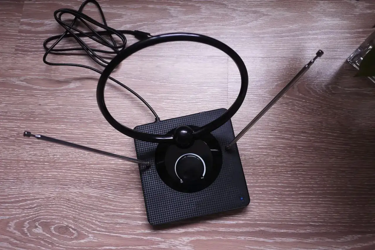 Antena DVB-T2/HEVC z okrągłą pętlą i teleskopowymi ramionami na drewnianym tle.