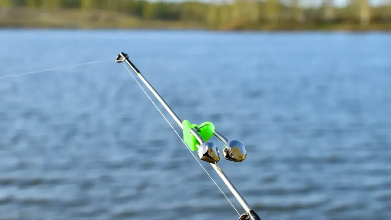 Wędka z zielonym sygnalizatorem brań i dwoma dzwoneczkami na tle wody.