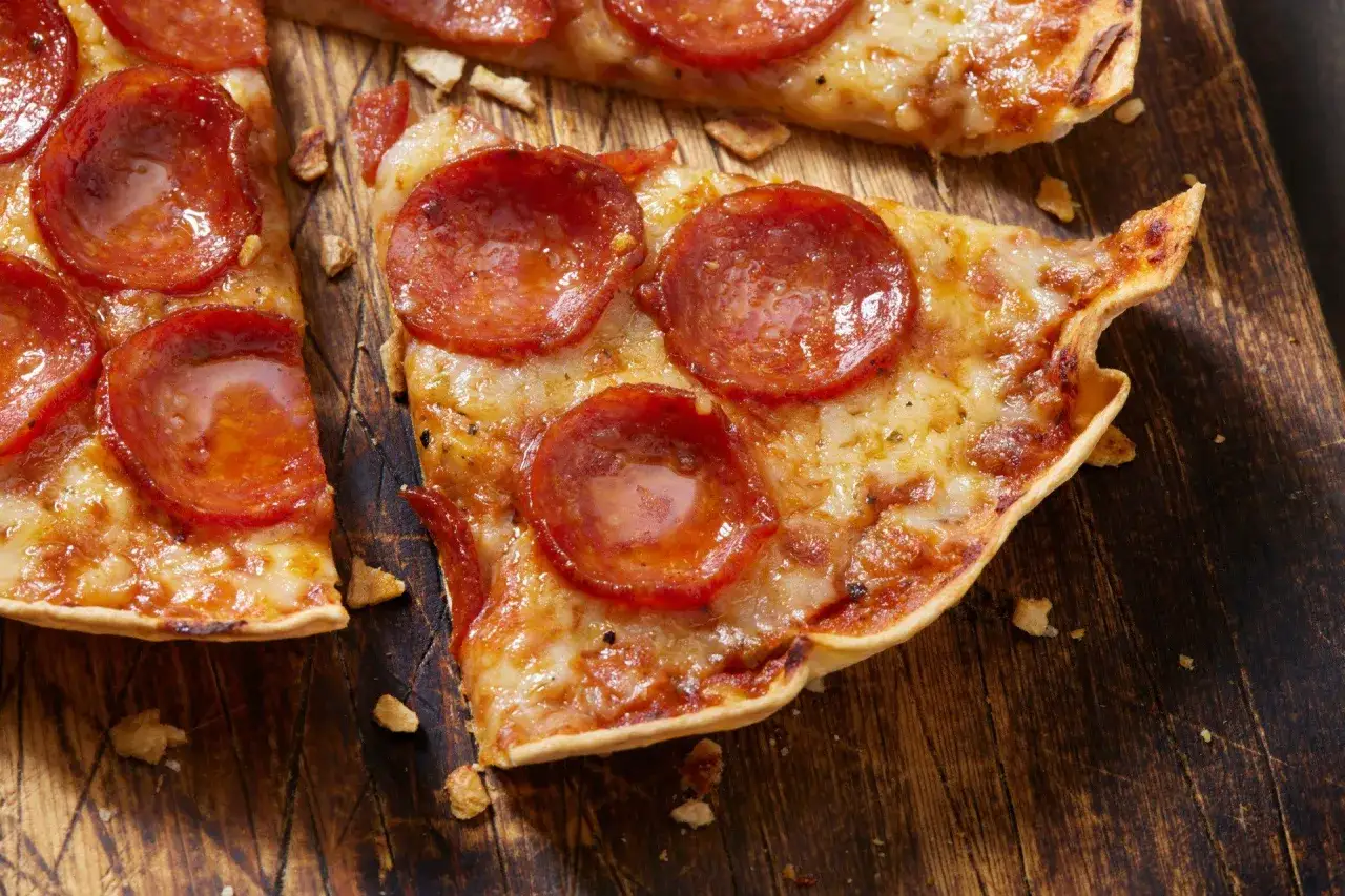 Pyszna pizza na tortilli z pepperoni, roztopionym serem i chrupiącym spodem, podana na drewnianej desce.