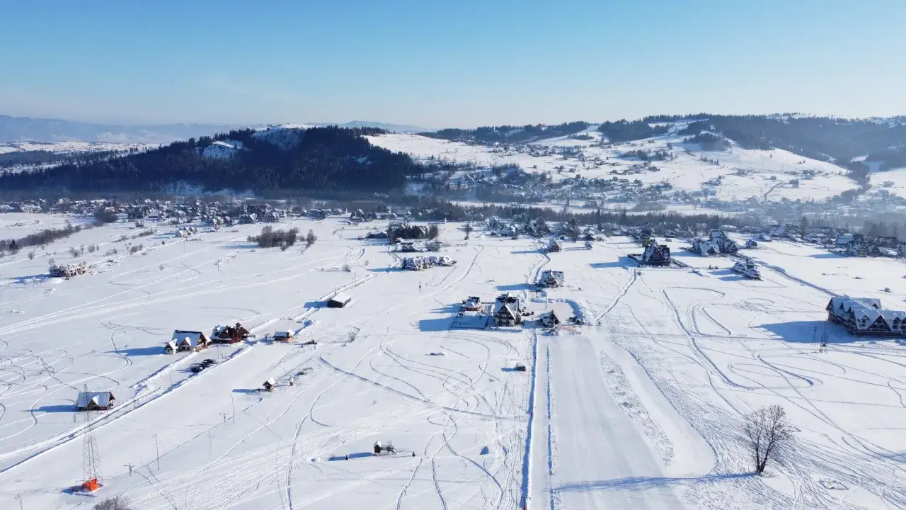Zimowy krajobraz z wyciągiem narciarskim Horników Wierch u Goryla. Śnieg pokrywa pola i dachy domów, tworząc malowniczy widok.