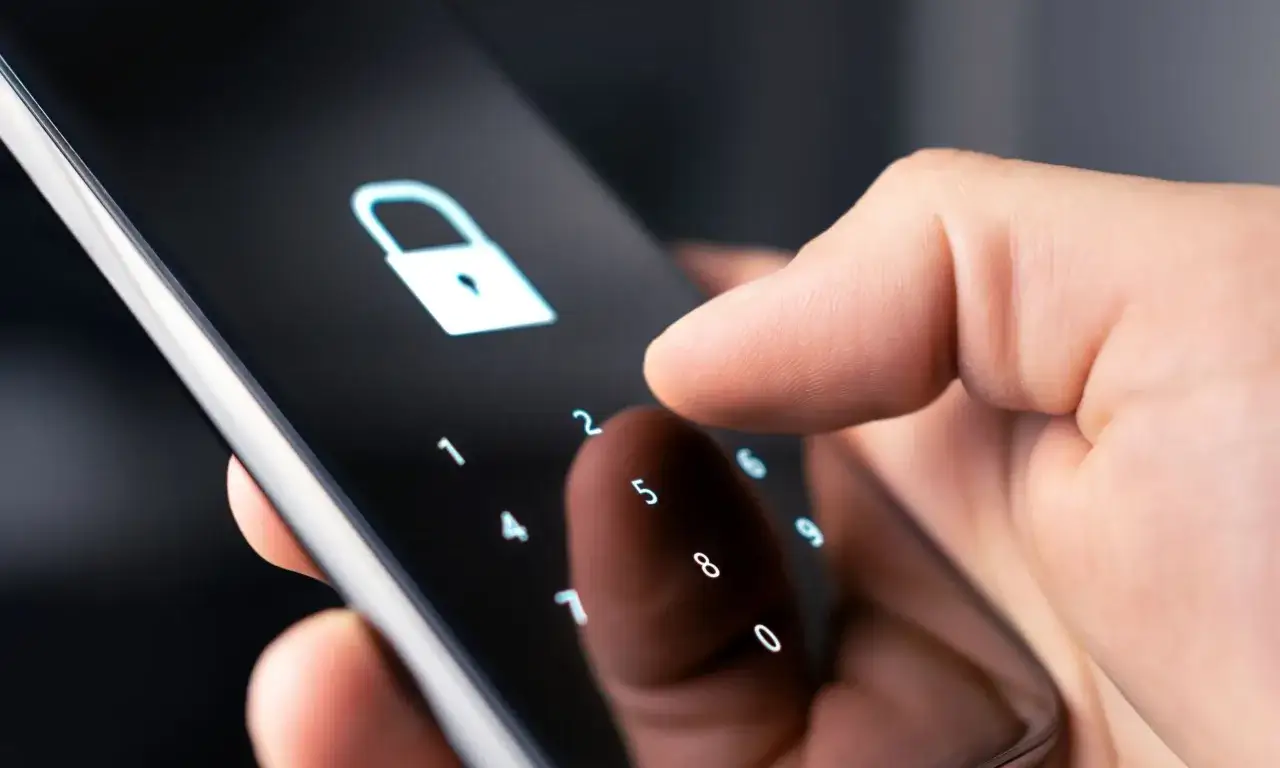 Dłoń wpisuje kod na ekranie telefonu, symbolizując jak zmienić kod w domofonie w bloku.