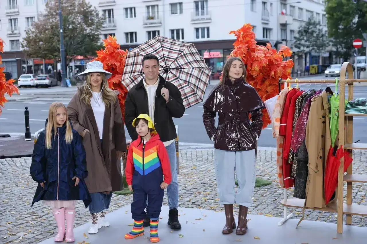Rodzina prezentuje stylowe stylizacje na deszczowe dni: płaszcze, kalosze i kolorowe parasole.