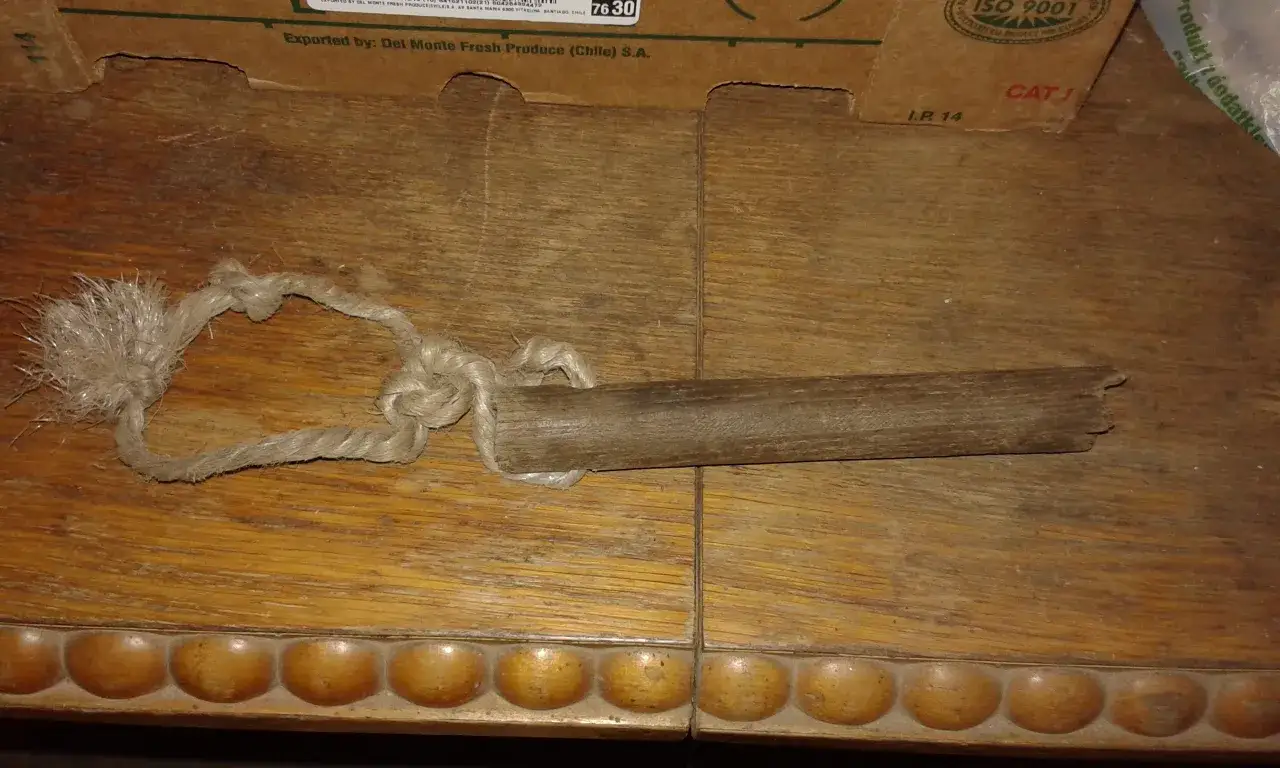 Drewniana dutka dla konia z grubą, plecioną liną. Przedmiot leży na drewnianym stole.