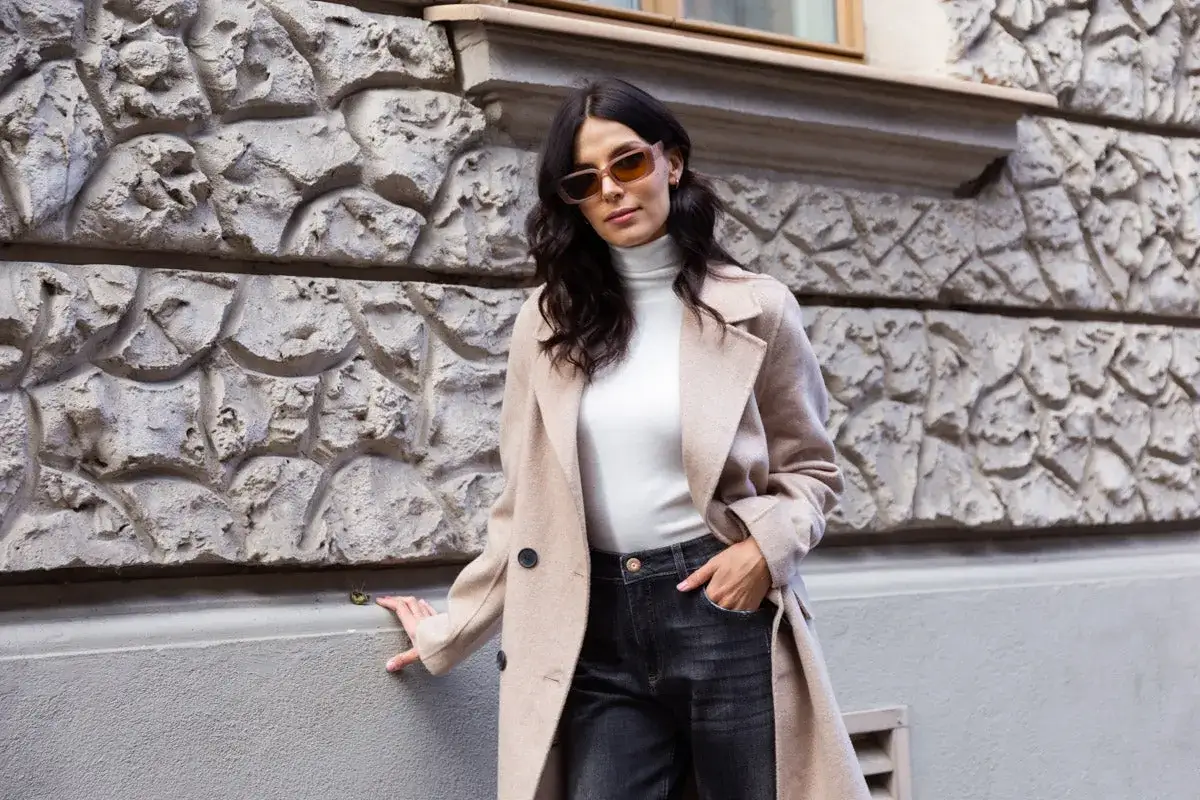Elegancka kobieta w beżowym płaszczu i ciemnych jeansach. Spódnica jeansowa midi stylizacje na co dzień.