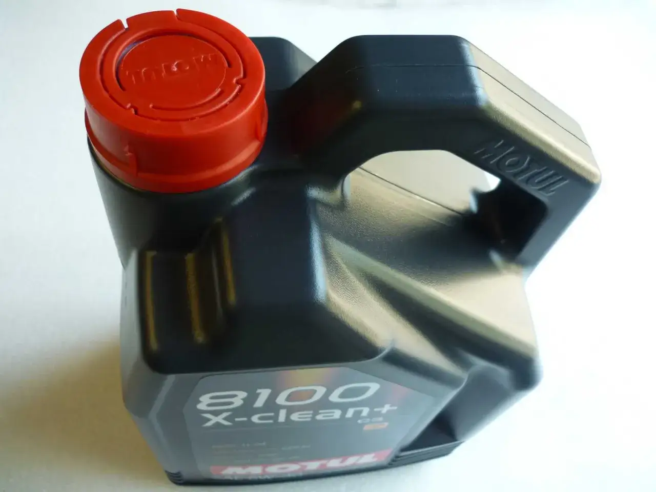 Czarny kanister z olejem silnikowym Motul 8100 X-clean+ z czerwoną zakrętką.