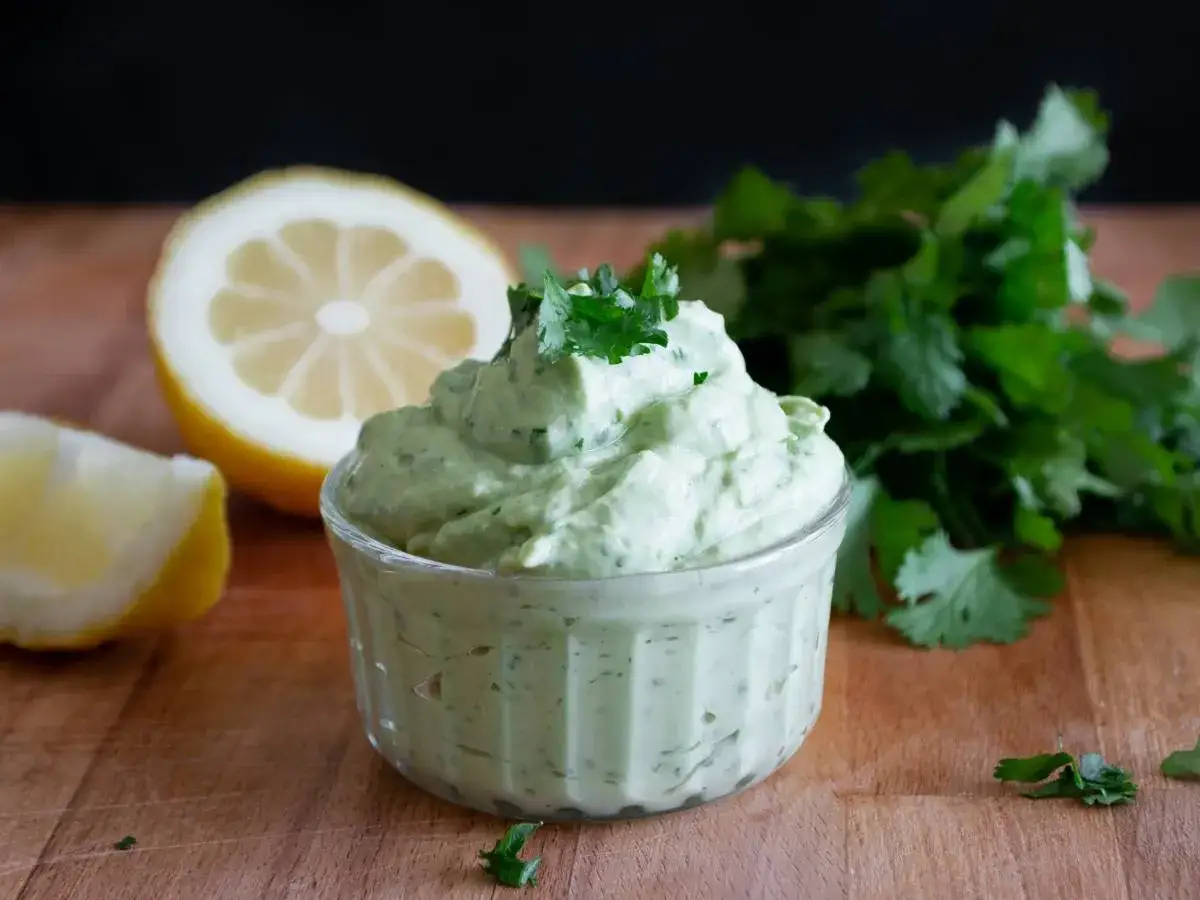 Zielony, kremowy sos śmietanowo ziołowy w miseczce, obok cytryny i świeżej kolendry.