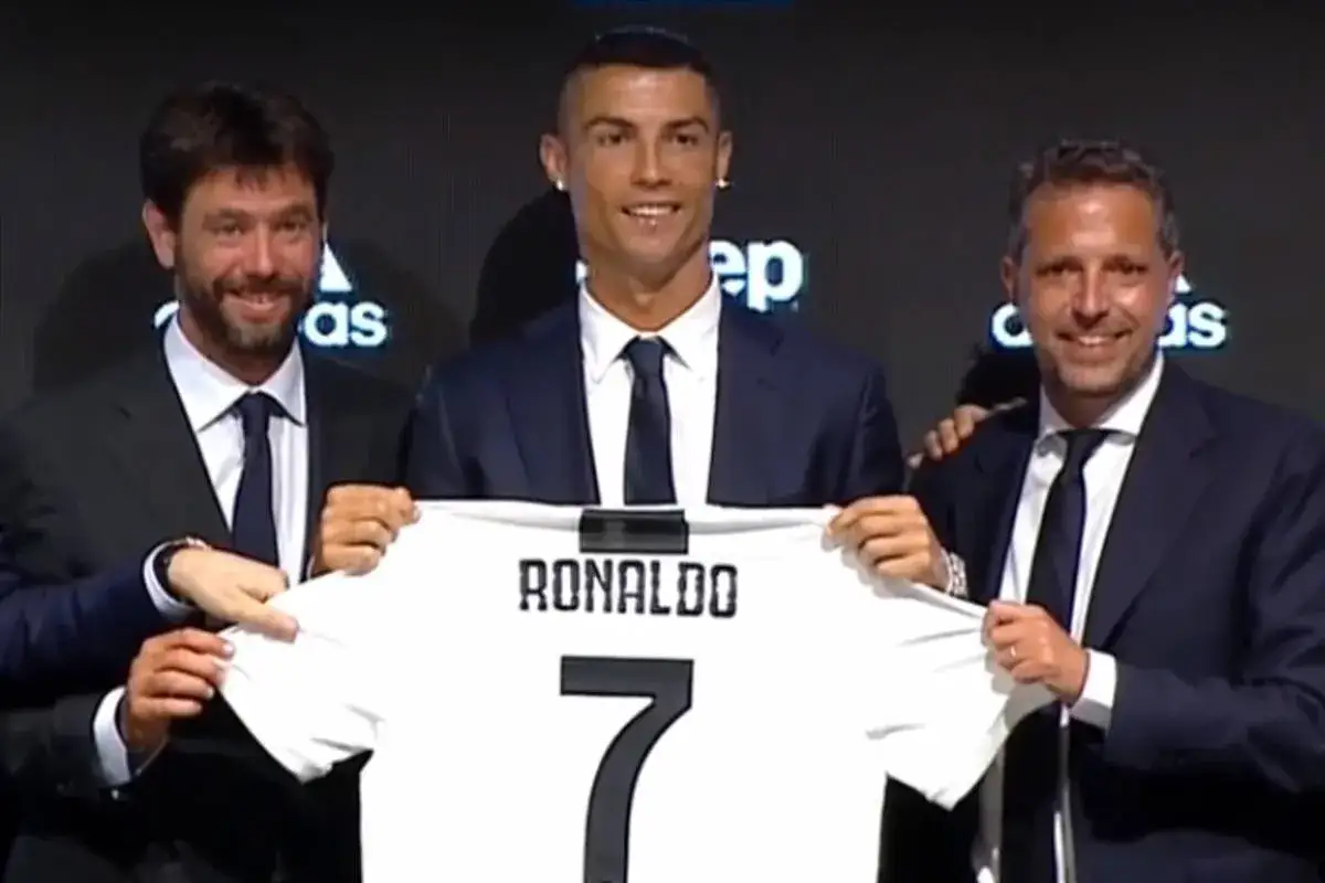 Cristiano Ronaldo z koszulką Juventusu z numerem 7, trzymaną przez niego i dwóch mężczyzn w garniturach.