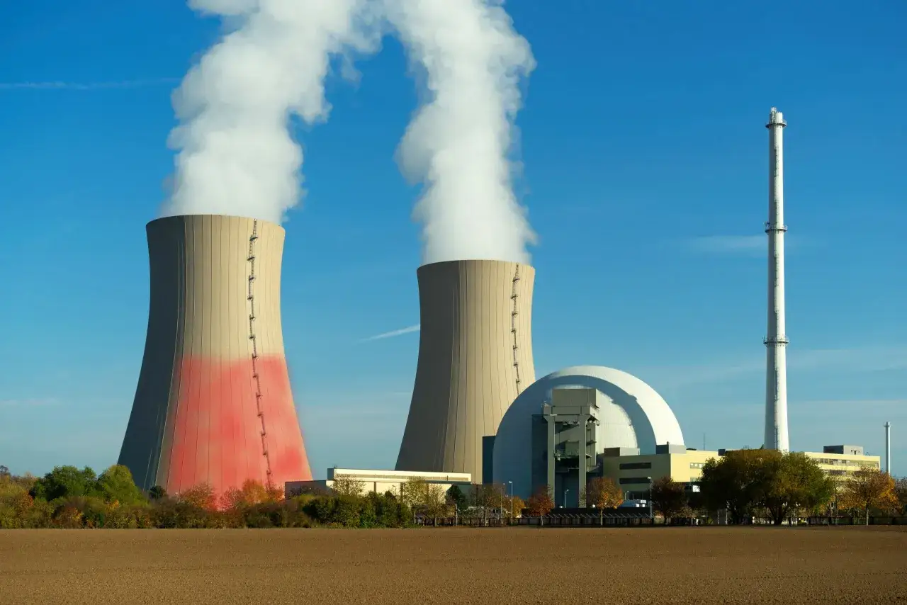 Dwie chłodnie kominowe i kopuła elektrowni konwencjonalnej na tle błękitnego nieba.