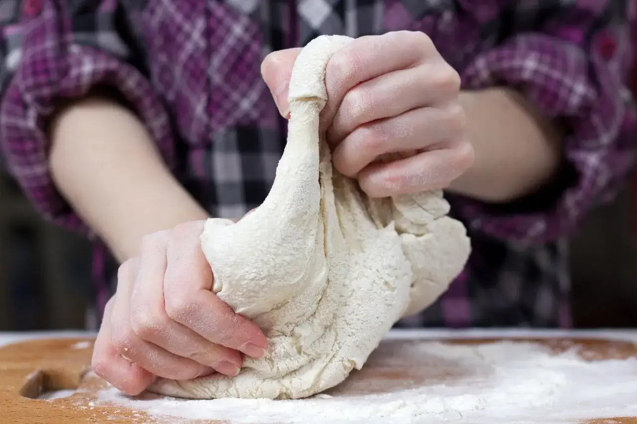 Ręce ugniatają masę solną na drewnianej desce. Dowiedz się, masa solna jak zrobić, by stworzyć własne dzieła.