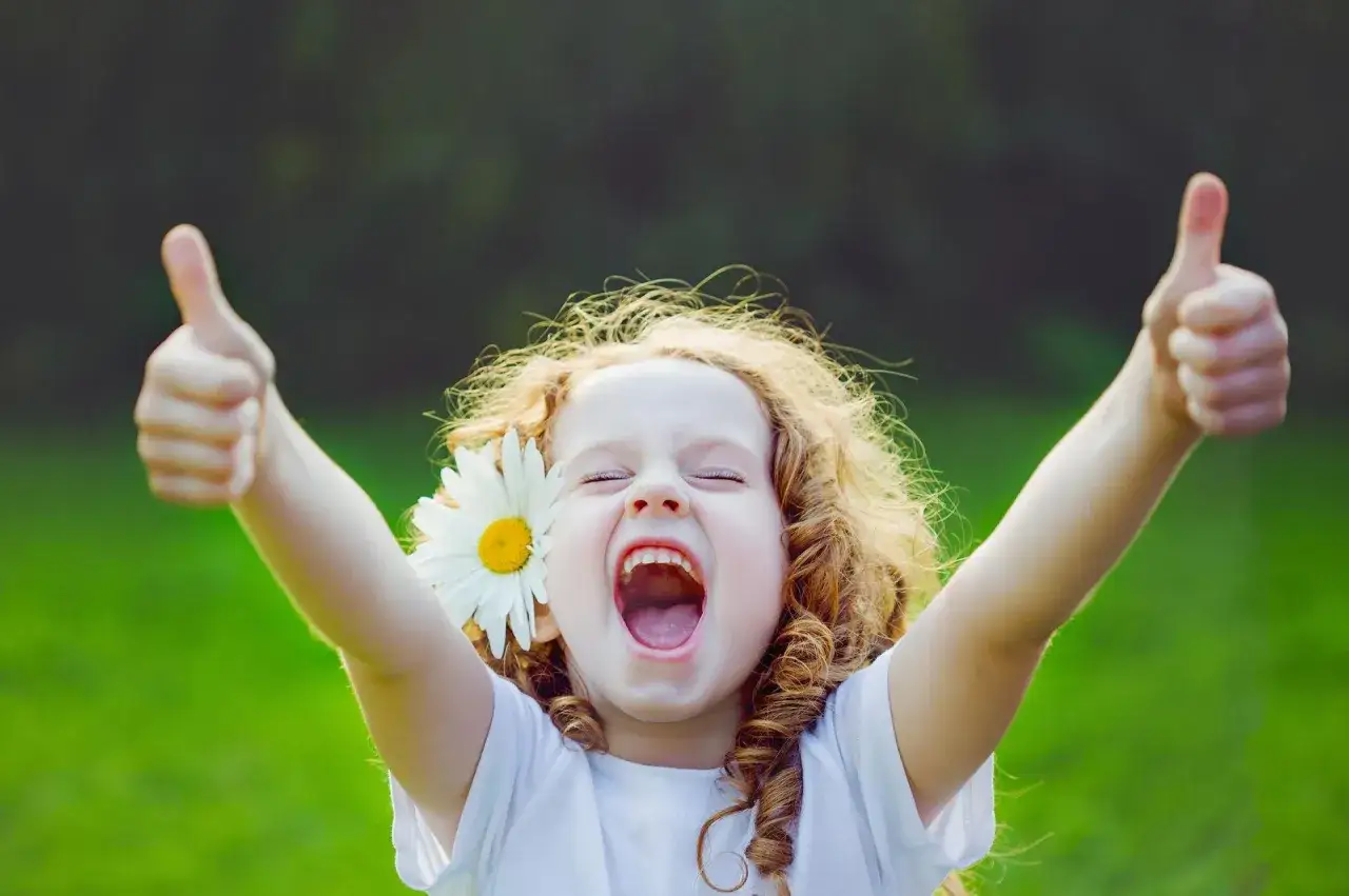 Szczęśliwa dziewczynka z rumiankiem we włosach pokazuje kciuki w górę.