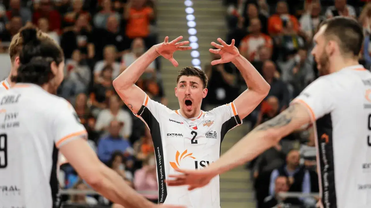 Siatkarz z numerem 2 na koszulce, z szeroko otwartymi ustami i rękami uniesionymi w geście zaskoczenia, na tle trybun. Wyniki tabeli ligi siatkówki mężczyzn.