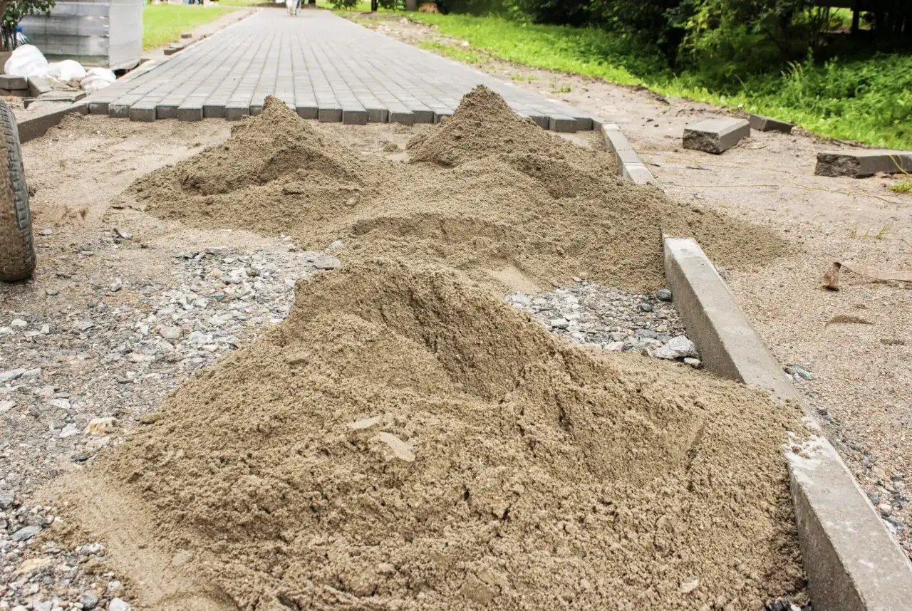 Kopce piasku czekają na ułożenie kostki brukowej. Trudno oszacować, ile piasku na m2 kostki, ale materiału jest sporo.