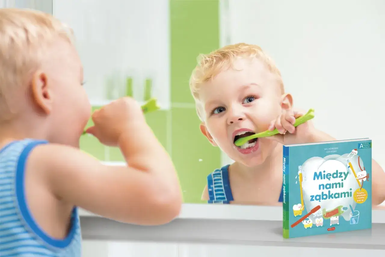Chłopiec myje ząbki przed lustrem, a obok leży książka "Między nami ząbkami", która odpowiada na pytanie, jak długo rusza się mleczak zanim wypadnie.