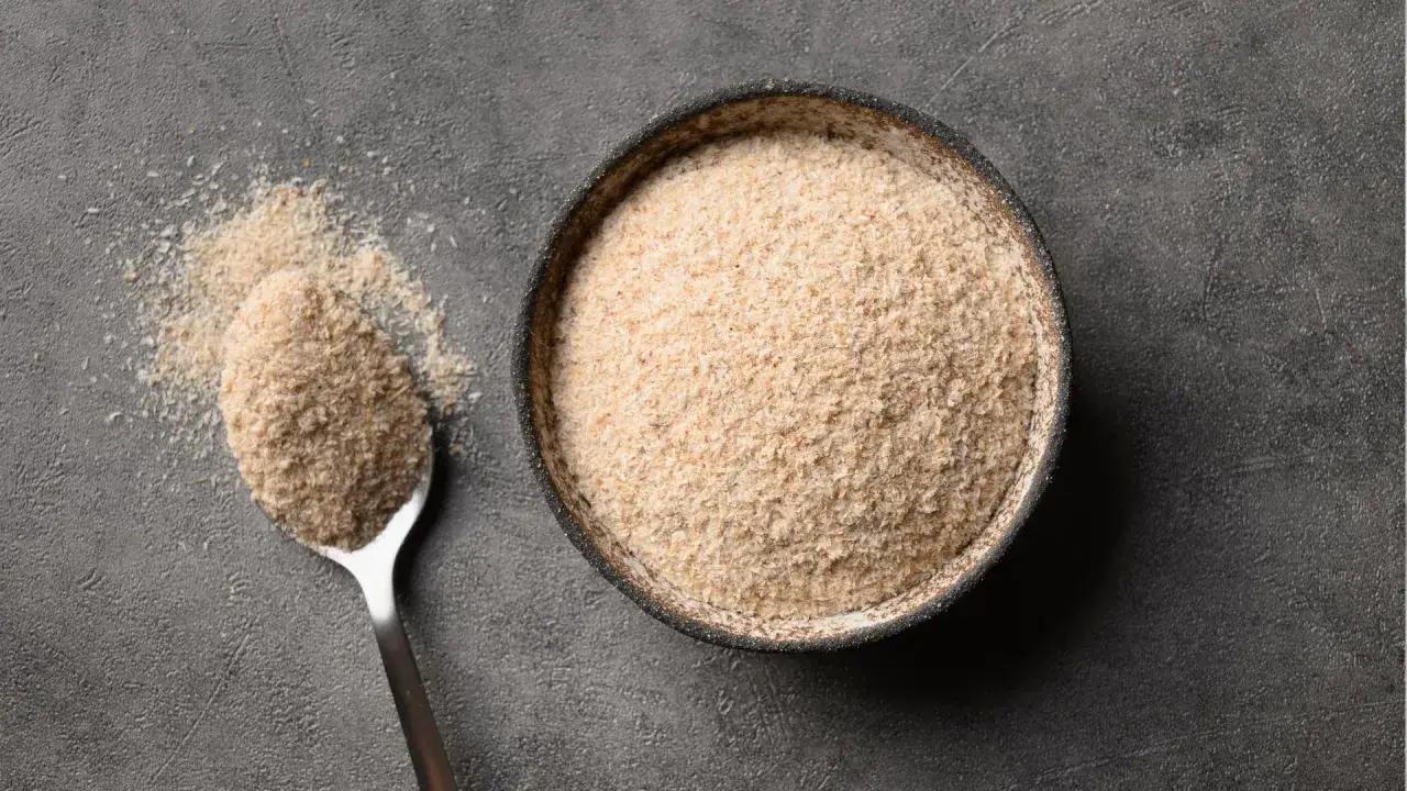 Łyżka i miska pełne jasnego proszku, który jest błonnikiem rozpuszczalnym w wodzie.