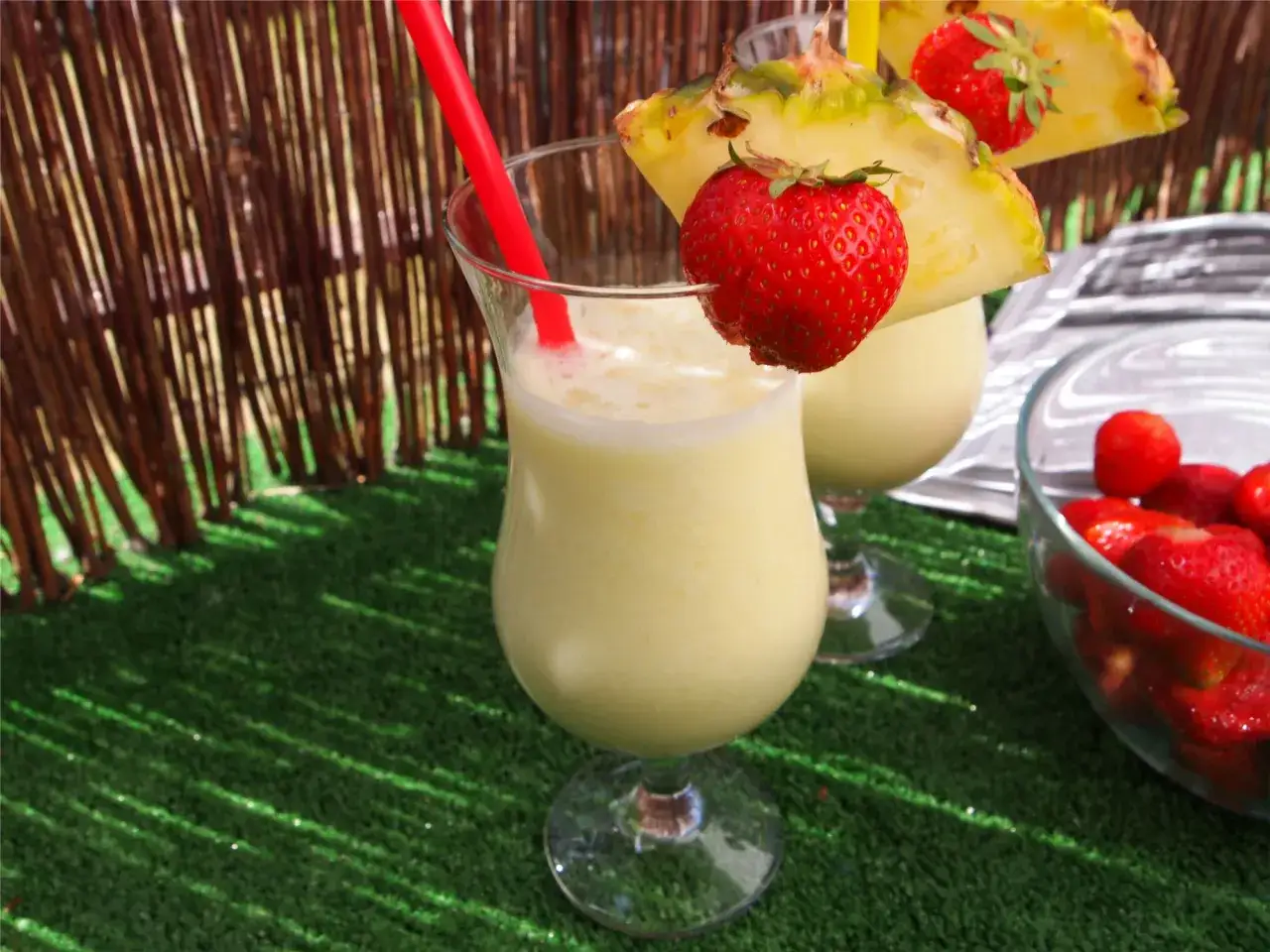 Dwa koktajle Pina Colada z ananasem i truskawkami na zielonej trawie.