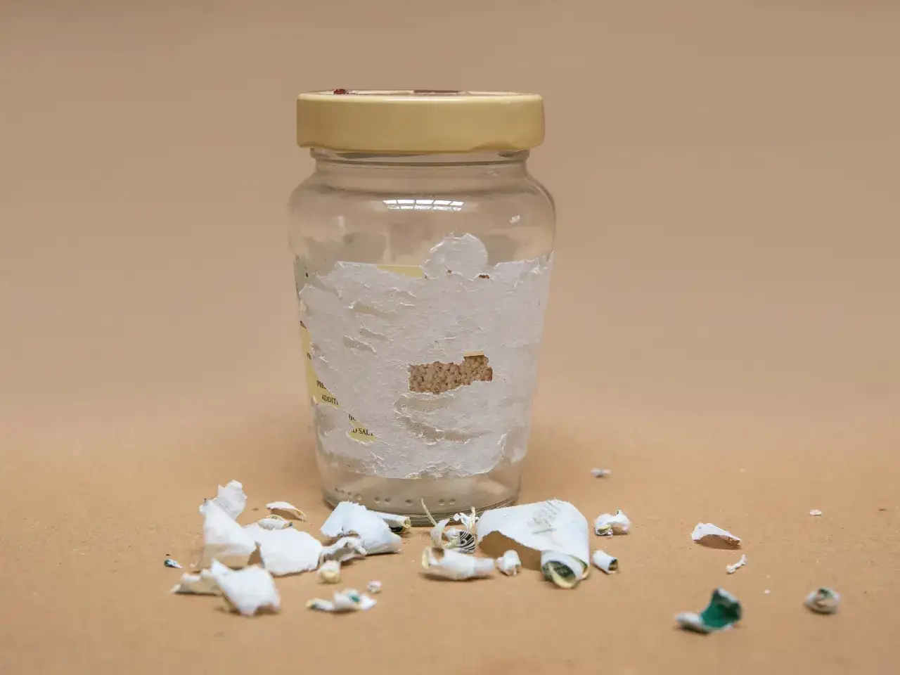 Szklana butelka z resztkami etykiety i oderwanymi fragmentami papieru na powierzchni.