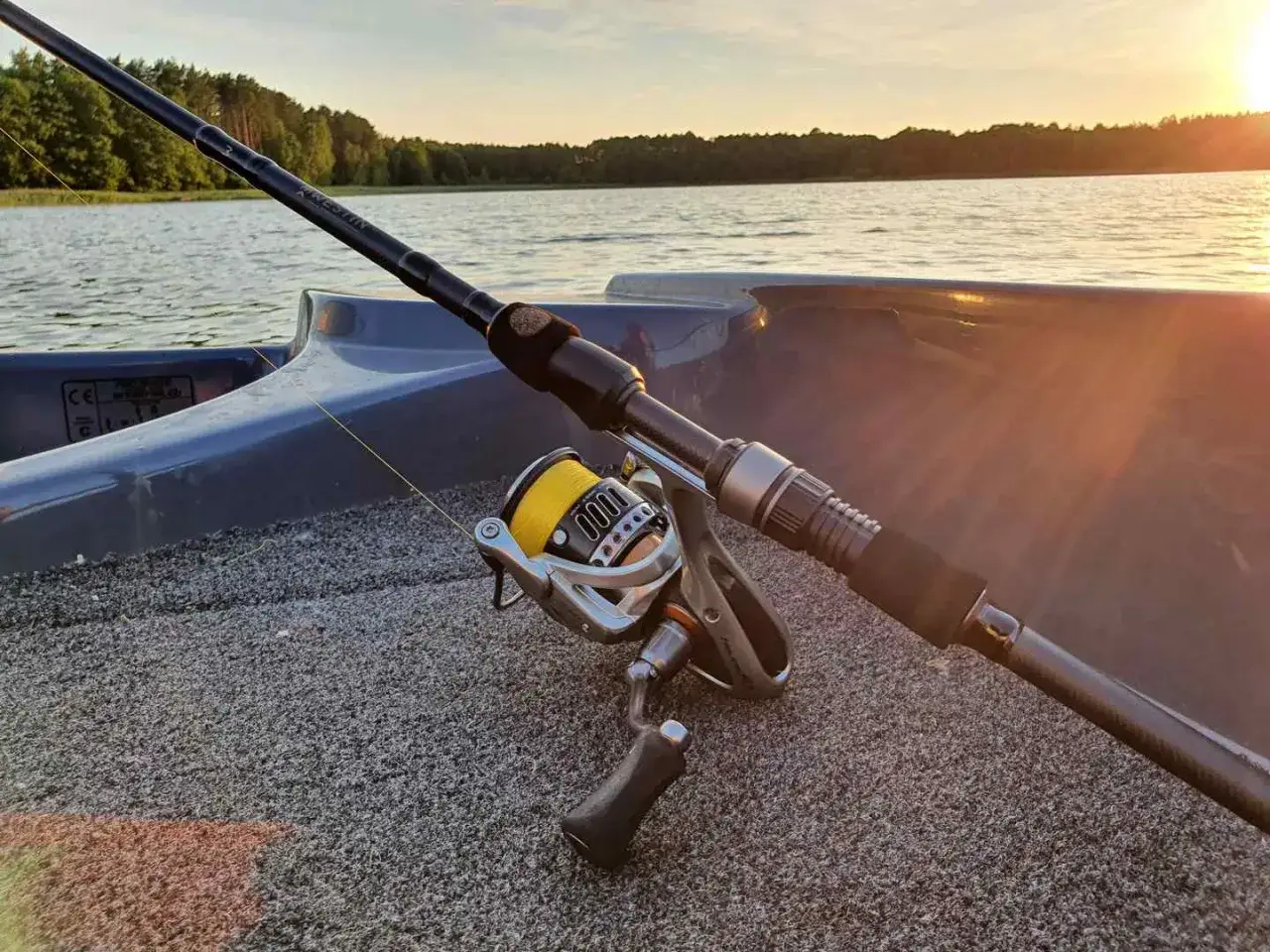Wędka na sandacza gotowa do akcji. Złoty zachód słońca nad jeziorem i sprzęt wędkarski w łodzi.
