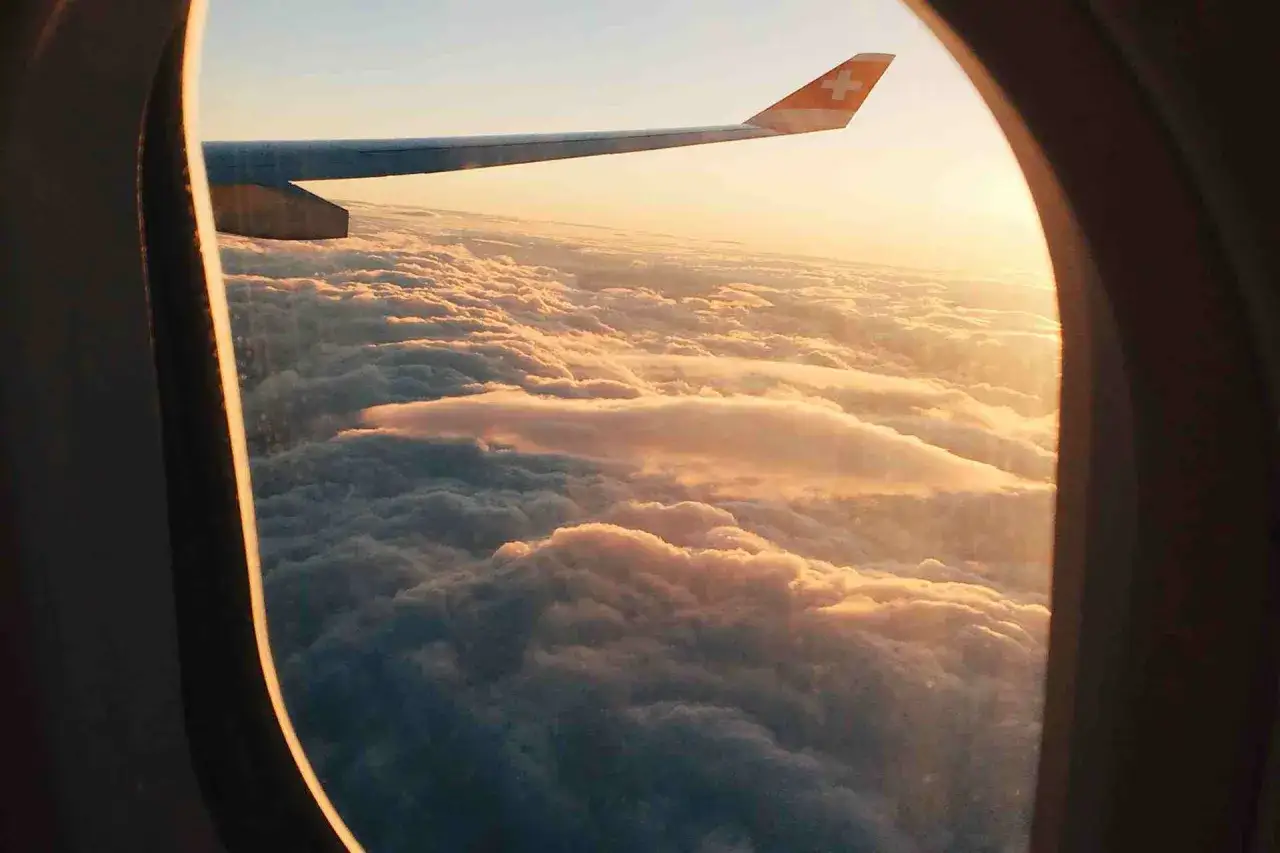 Widok z okna samolotu na chmury o zachodzie słońca, widoczne skrzydło samolotu.
