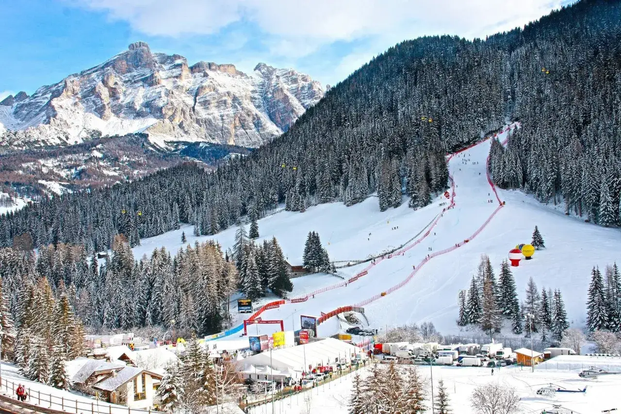 Ośnieżony stok narciarski w Alta Badia z lasem i górami w tle.