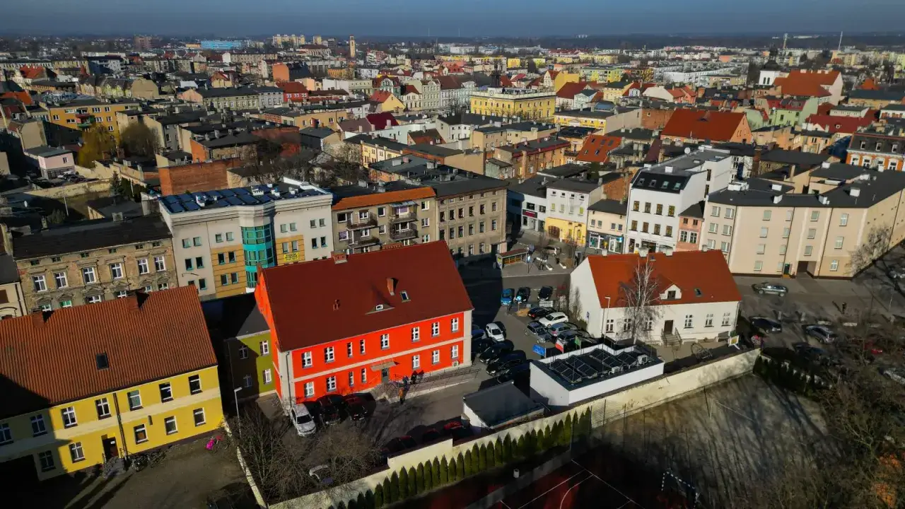 Widok z lotu ptaka na miasto, gdzie leży Ostrów Wielkopolski. Widać kolorowe kamienice, dachy i samochody.