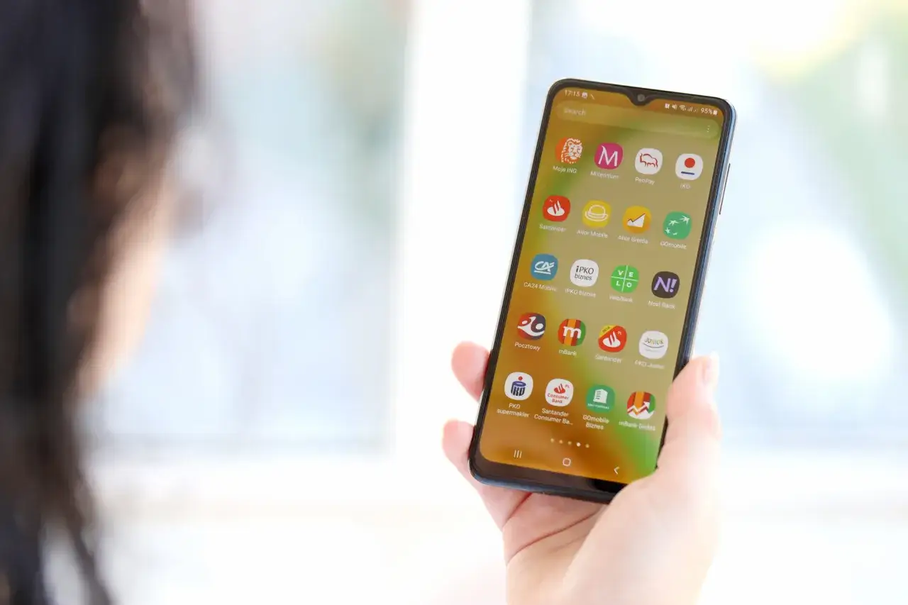 Dłoń trzyma smartfon z ikonami aplikacji bankowych. Widoczna ikona mBank, pomocna przy pytaniu jak zmienic numer telefonu mbank.