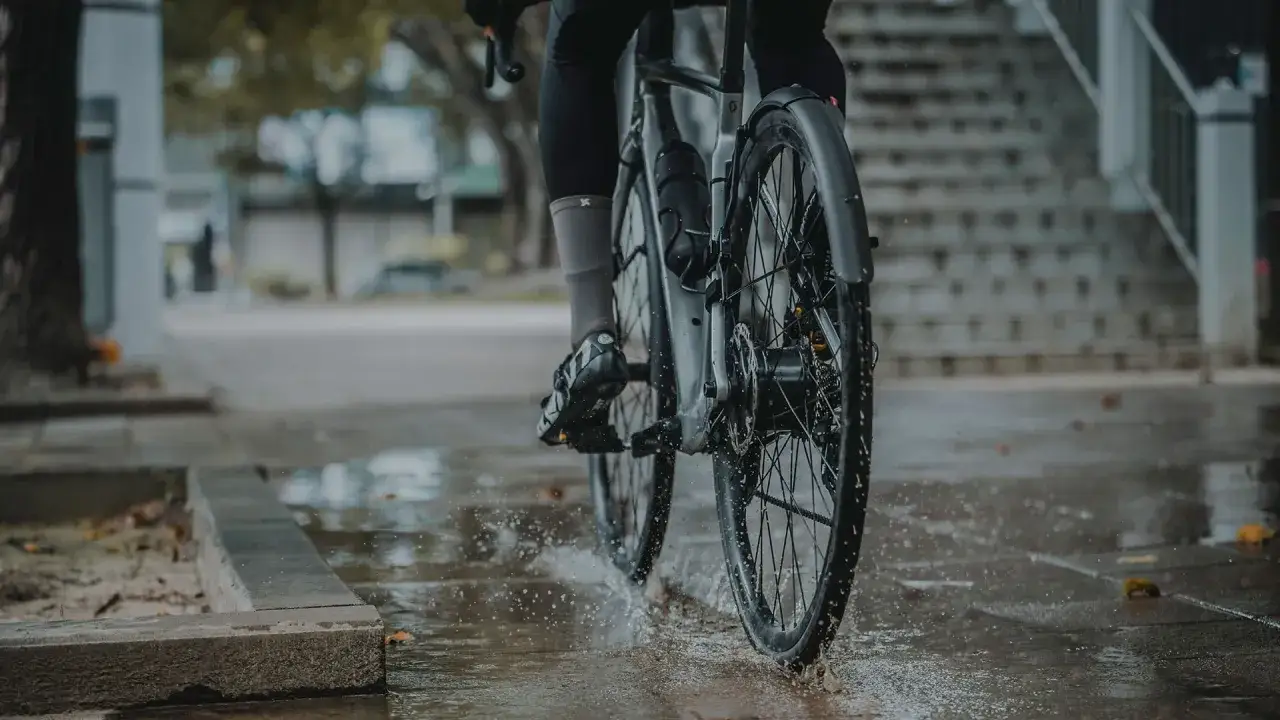 Rowerzysta w deszczu, koła rozpryskują wodę. Montaż błotnika rowerowego zapewnia suchą jazdę.