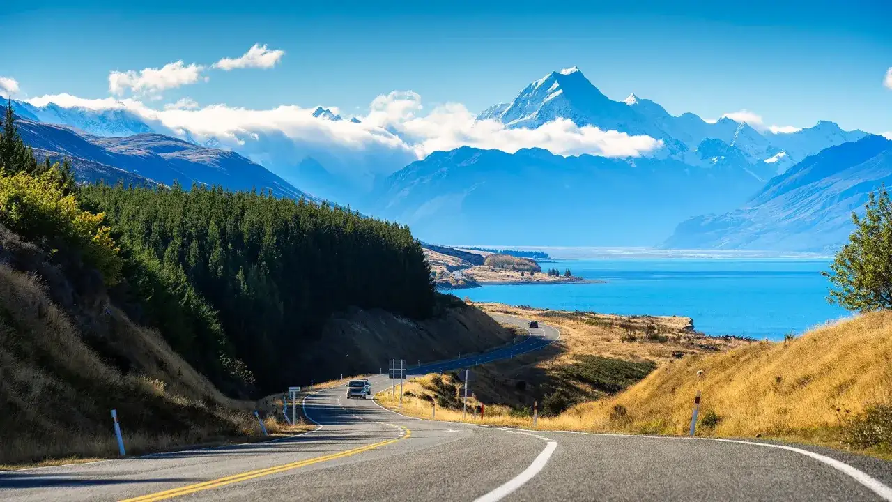 Malownicza droga w Nowej Zelandii prowadzi do turkusowego jeziora i ośnieżonych gór. Idealna temperatura na zwiedzanie.