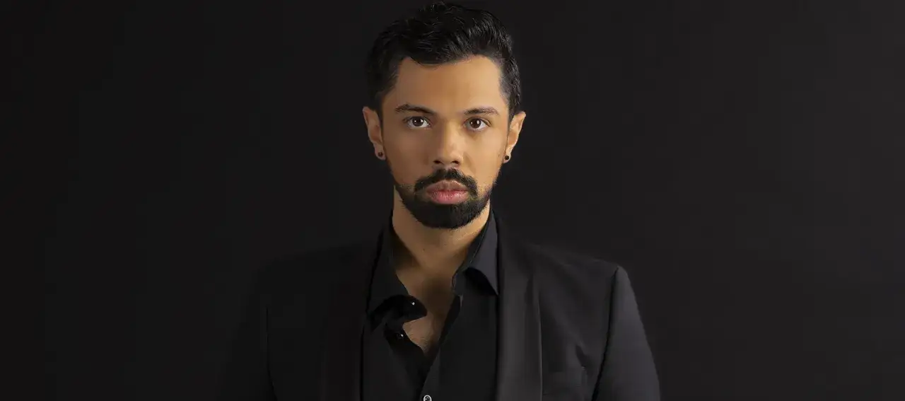 Mężczyzna w czarnym garniturze, z zarostem i kolczykiem w uchu. Jego spojrzenie sugeruje, że posiada najwyższy głos męski.