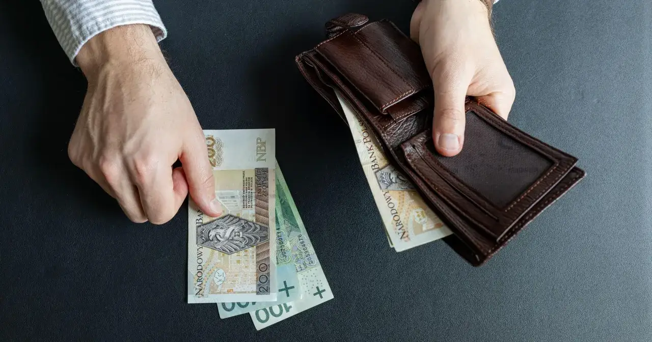 Ręce trzymają polskie banknoty i brązowy portfel. Czy to początek wzrostu renty alkoholowej o 5% od marca 2026?