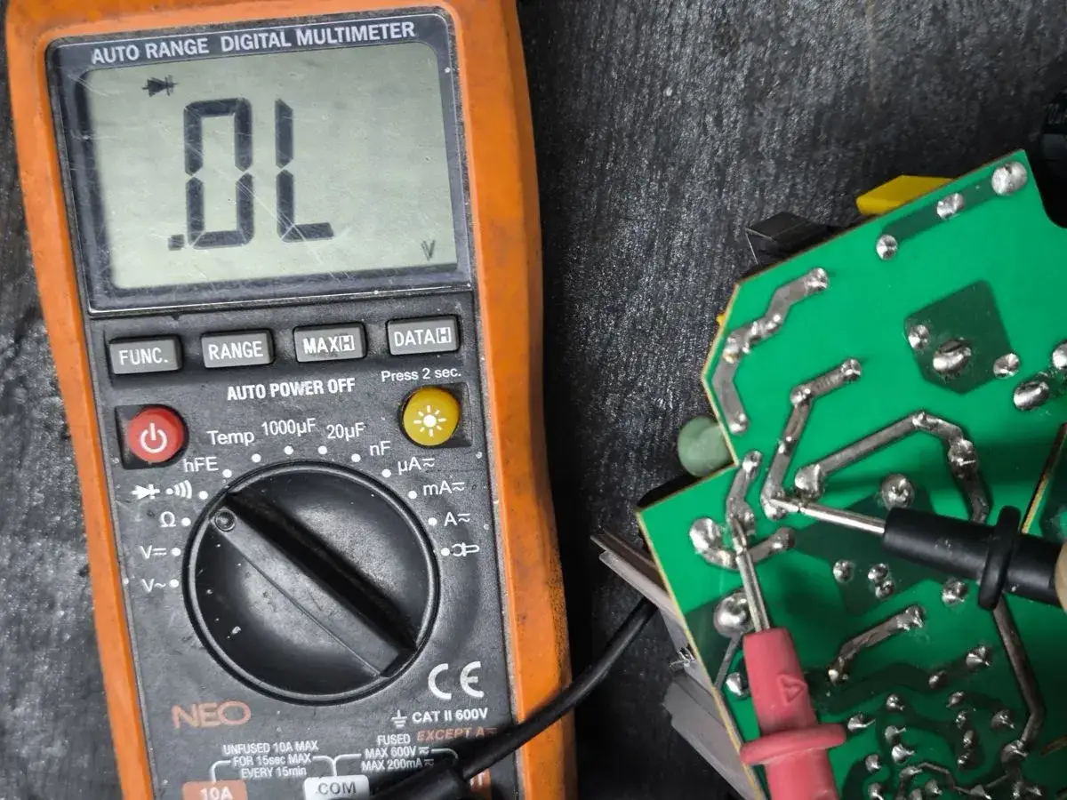 Pomarańczowy multimetr z wyświetlaczem "OL" obok zielonej płytki drukowanej z sondami.